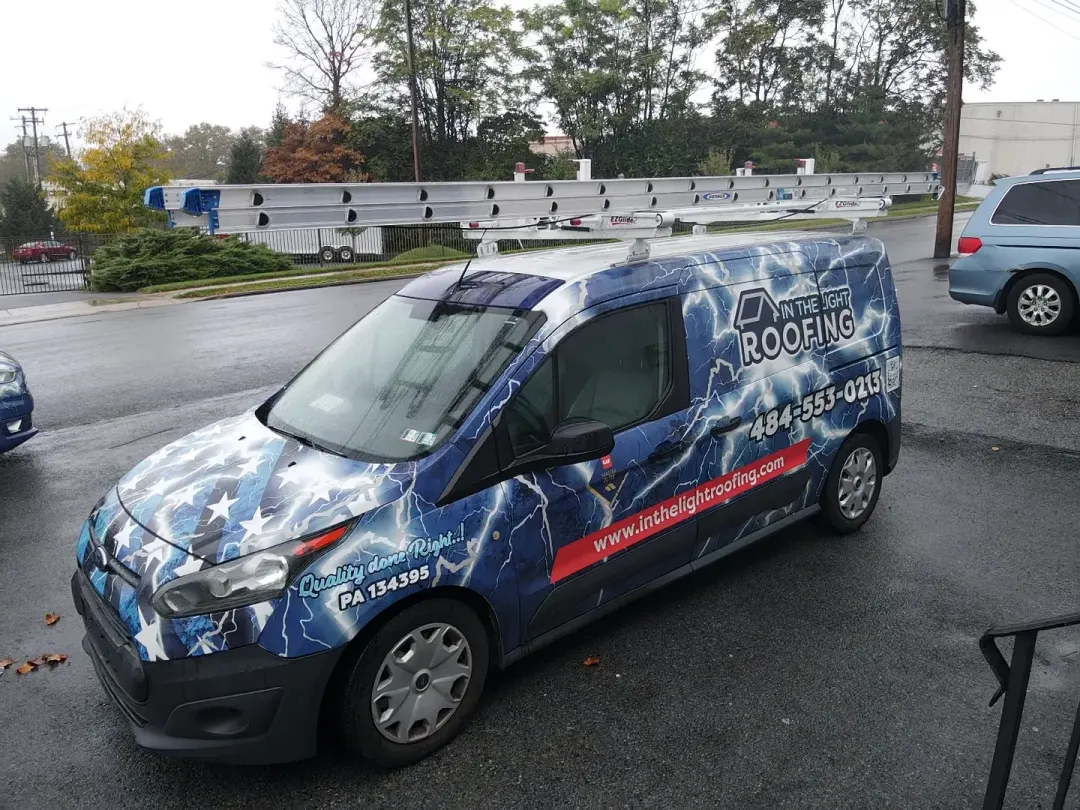 An In The Light Roofing van with ladders on the roof rack, parked outside the shop