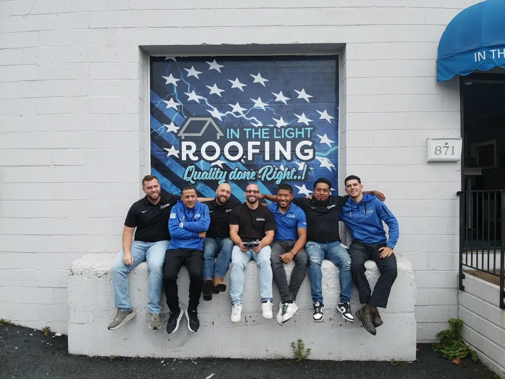 The In The Light Roofing crew sitting on the wall outside the shop in Allentown, under the company mural
