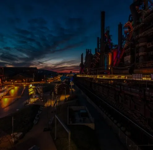 Lehigh Valley service area: floodlit blast furnaces and smokestacks of a steel plant standing above a lit street at dusk