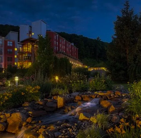 Macungie service area: a lit red brick building on a wooded hillside above a landscaped rock stream at night