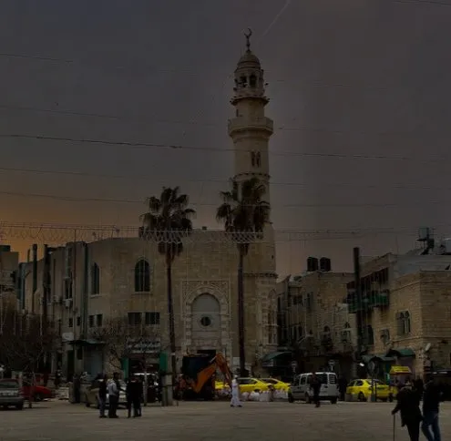 Bethlehem service area: a stone mosque with a tall minaret standing over a busy square lined with palm trees