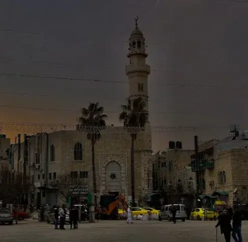 Bethlehem service area: a stone mosque with a tall minaret standing over a busy square lined with palm trees