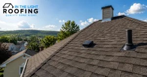 Dark asphalt shingle roof with a chimney and roof vents, houses and wooded hills behind